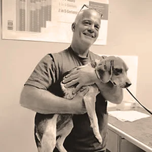 Veterinarian Dr. Jon S. Laing smiles while holding a medium-sized dog during an exam.
