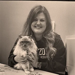 Dr. Mackenzie Holmes smiling while holding a fluffy cat, in a sepia-toned photo.