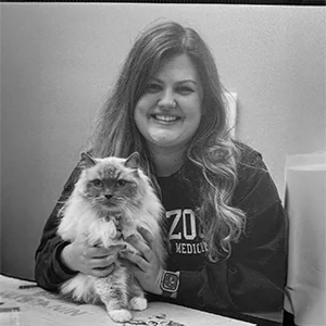 Dr. Mackenzie Holmes smiling while holding a fluffy cat, in a black and white photo.